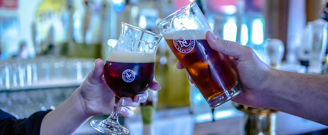 Two people toasting glasses of our beer at the bar in The Pub