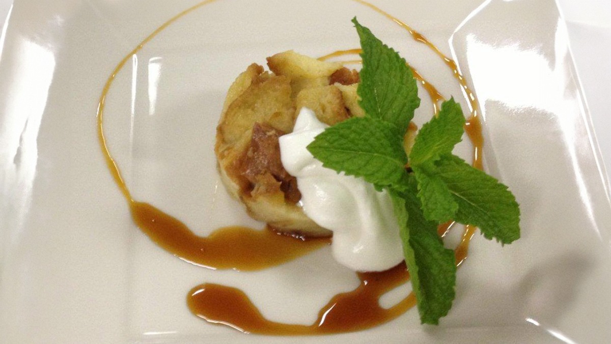 One serving of bread pudding on a plate, garnished with whipped cream and a mint sprig, and drizzled with Old Stock Ale reduction sauce.