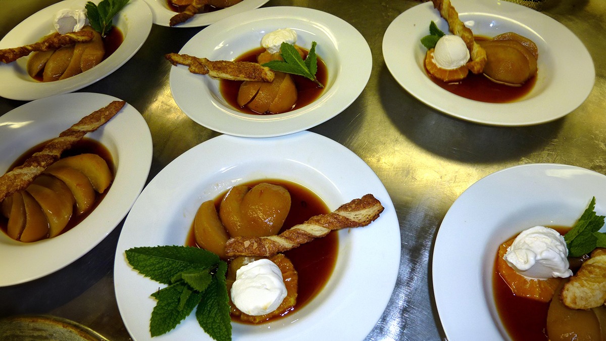 Six plates, each with a sliced poached pear, Old Stock Ale reduction, whipped cream, mint sprig, and cinnamon twist.