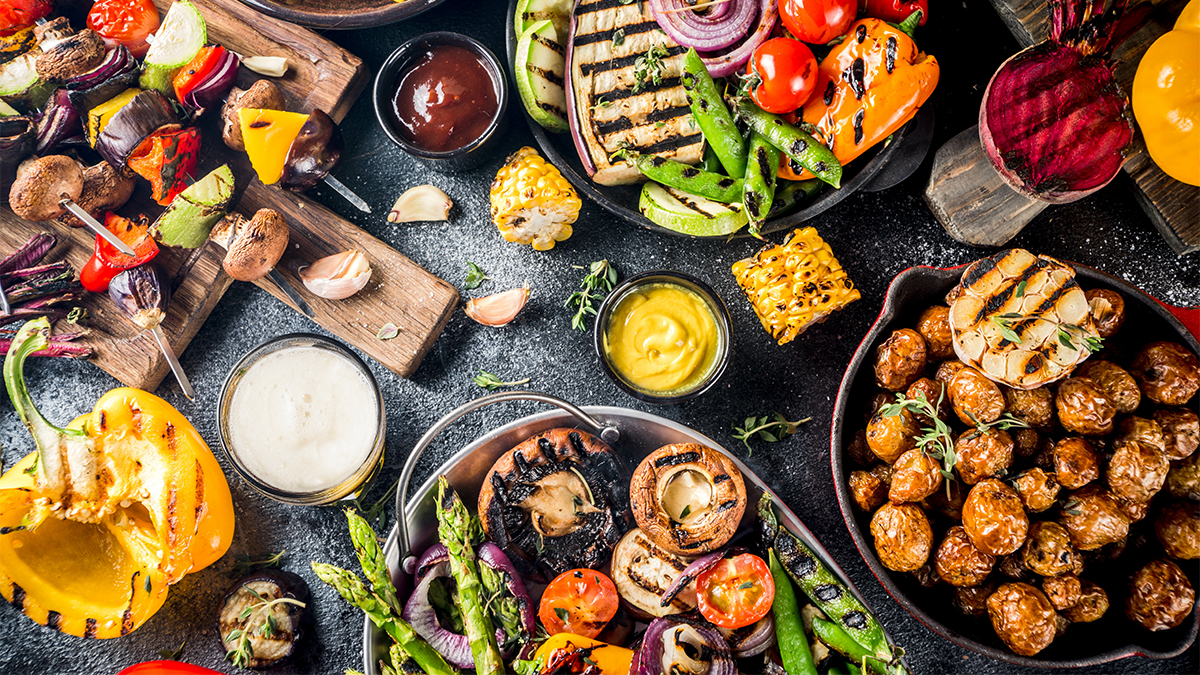 BBQ veggies laid out on a table with a glass of beer and sauces.