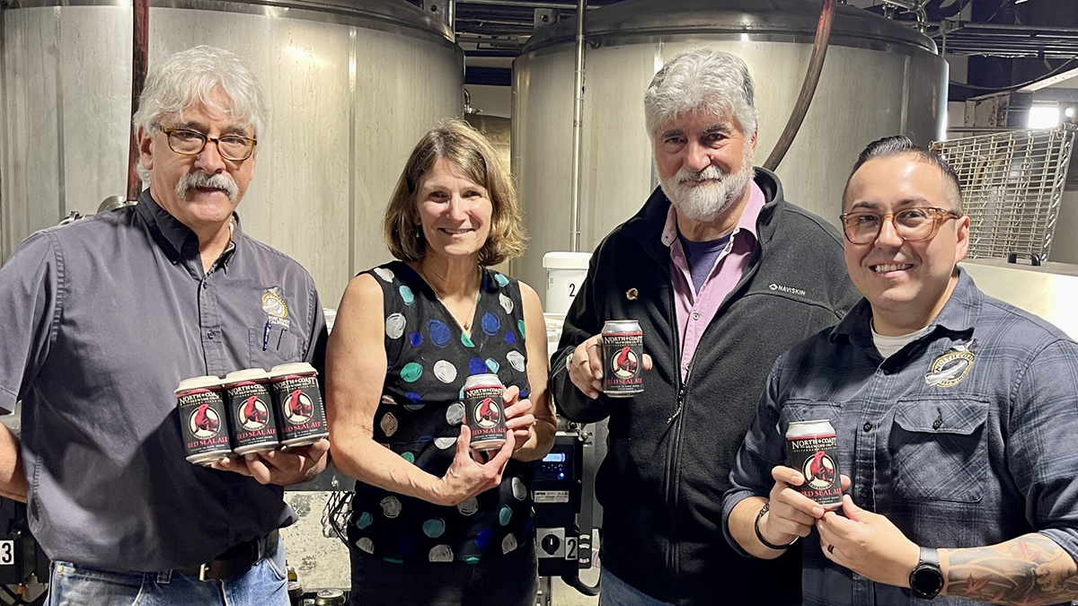 From left to right: Brewmaster Chuck Martins, CEO Jennifer Owen, Founding Brewmaster Mark Ruedrich, and Assistant Brewmaster Obed Salazar holding Red Seal Ale beer cans fresh off the canning line.