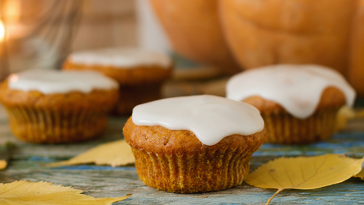 Four spiced cupcakes with glaze topping sitting on a table with fall leaves.