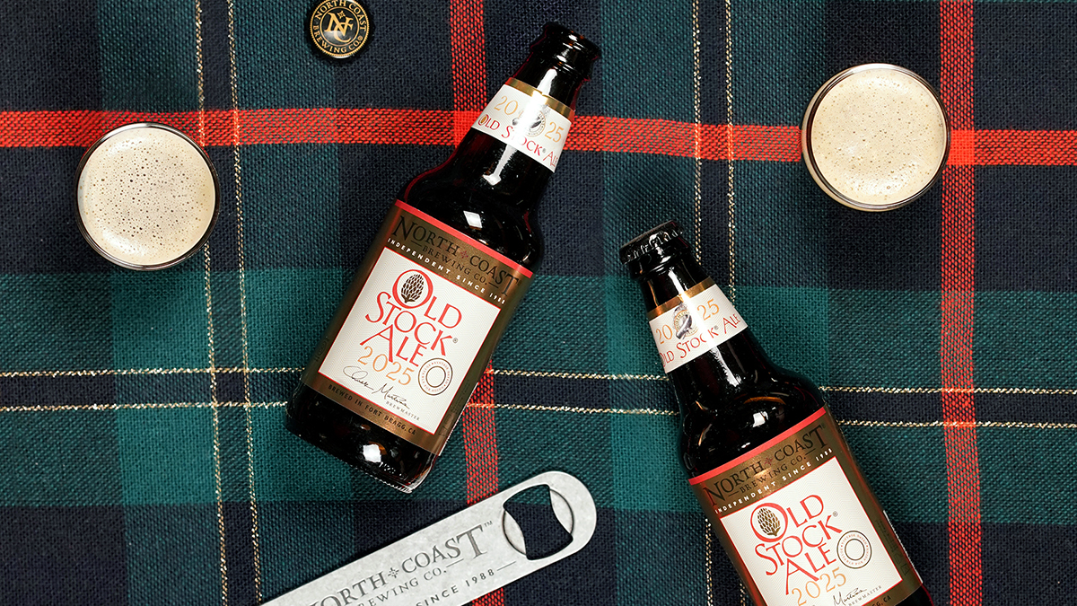 Overhead view of two small glasses of beer with bottles of Old Stock Ale and a North Coast brewing Co. Bottle opener on a green and red plaid tablecloth.
