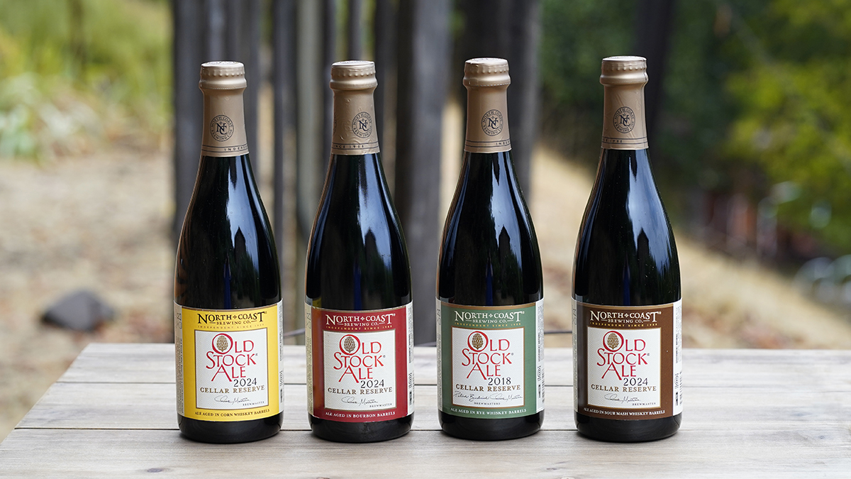 Four different 500ml bottles of Old Stock Ale Cellar Reserve each aged in a different spirit barrel, sitting on a picnic table outdoors.