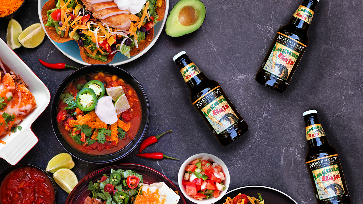 Top view of Mexican food spread, with three bottles of Laguna Baja.