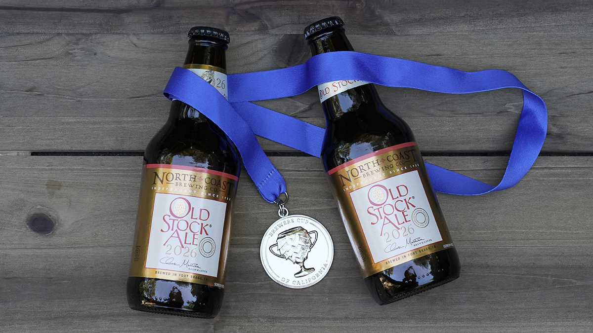 Two bottles of Old Stock Ale lay on a picnic table draped with a silver medal from the Brewers Cup of California.