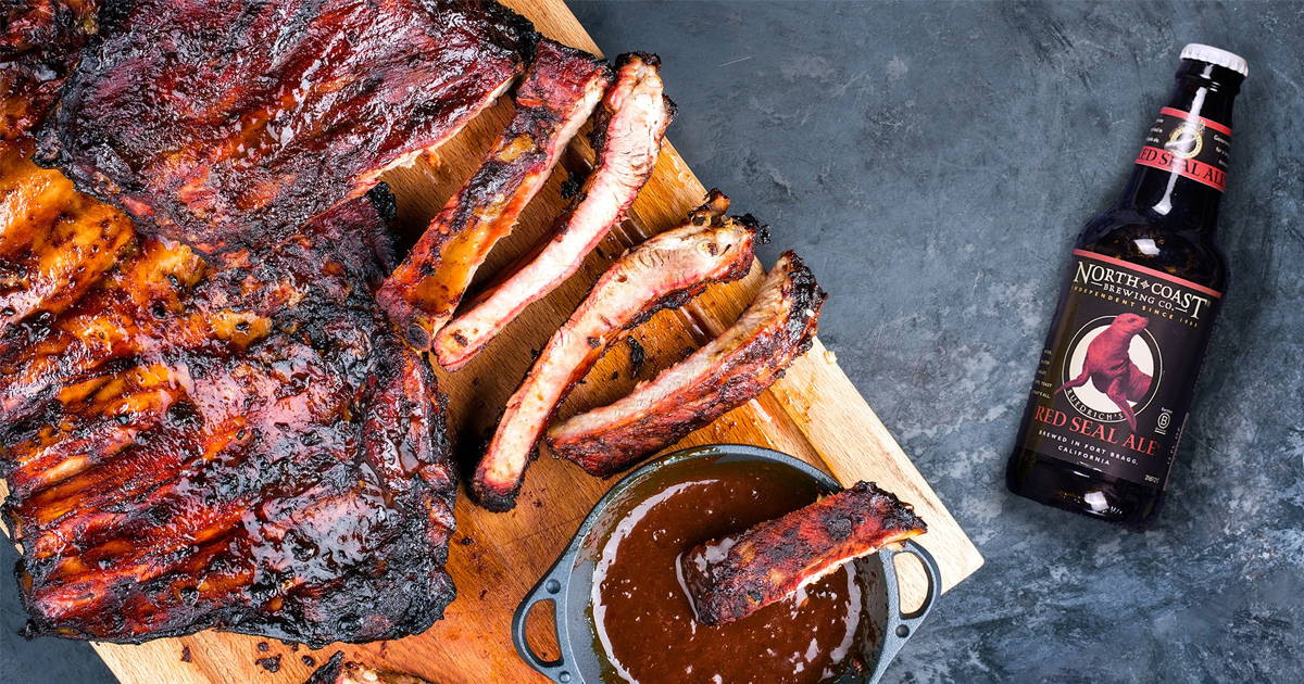 Top view of a bottle of Red Seal Ale laying next to a rack of ribs with barbecue sauce.