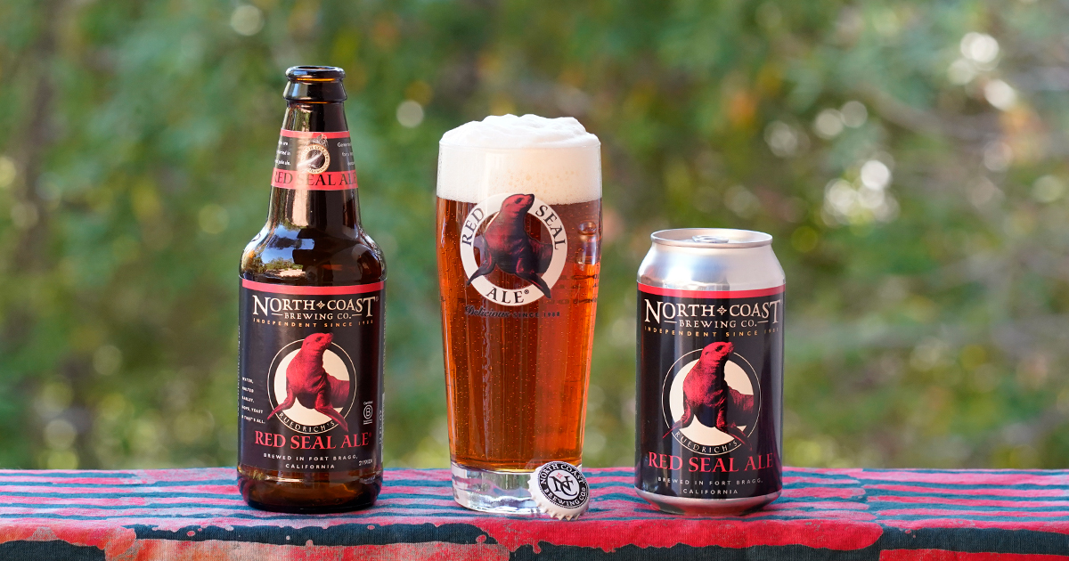 Red Seal Ale bottle and can with glass of the beer on a tablecloth outdoors.