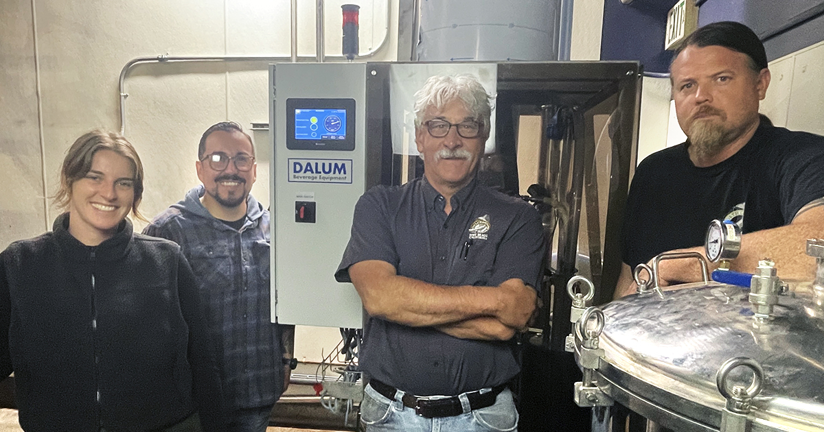 Four people standing around the Dalum CO2 capture unit at the brewery.