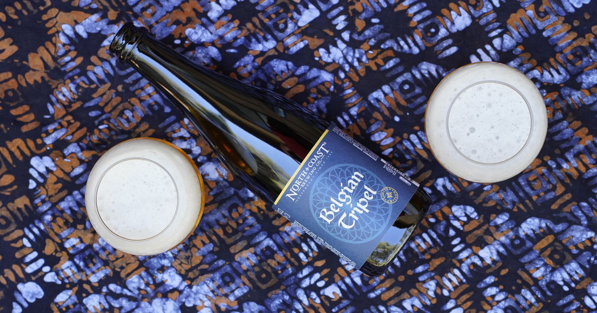 A 500ml bottle of Belgian Tripel laying on a table with two glasses of beer.